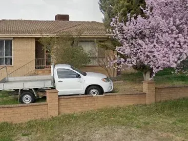 A white truck is parked in front of a brick house.