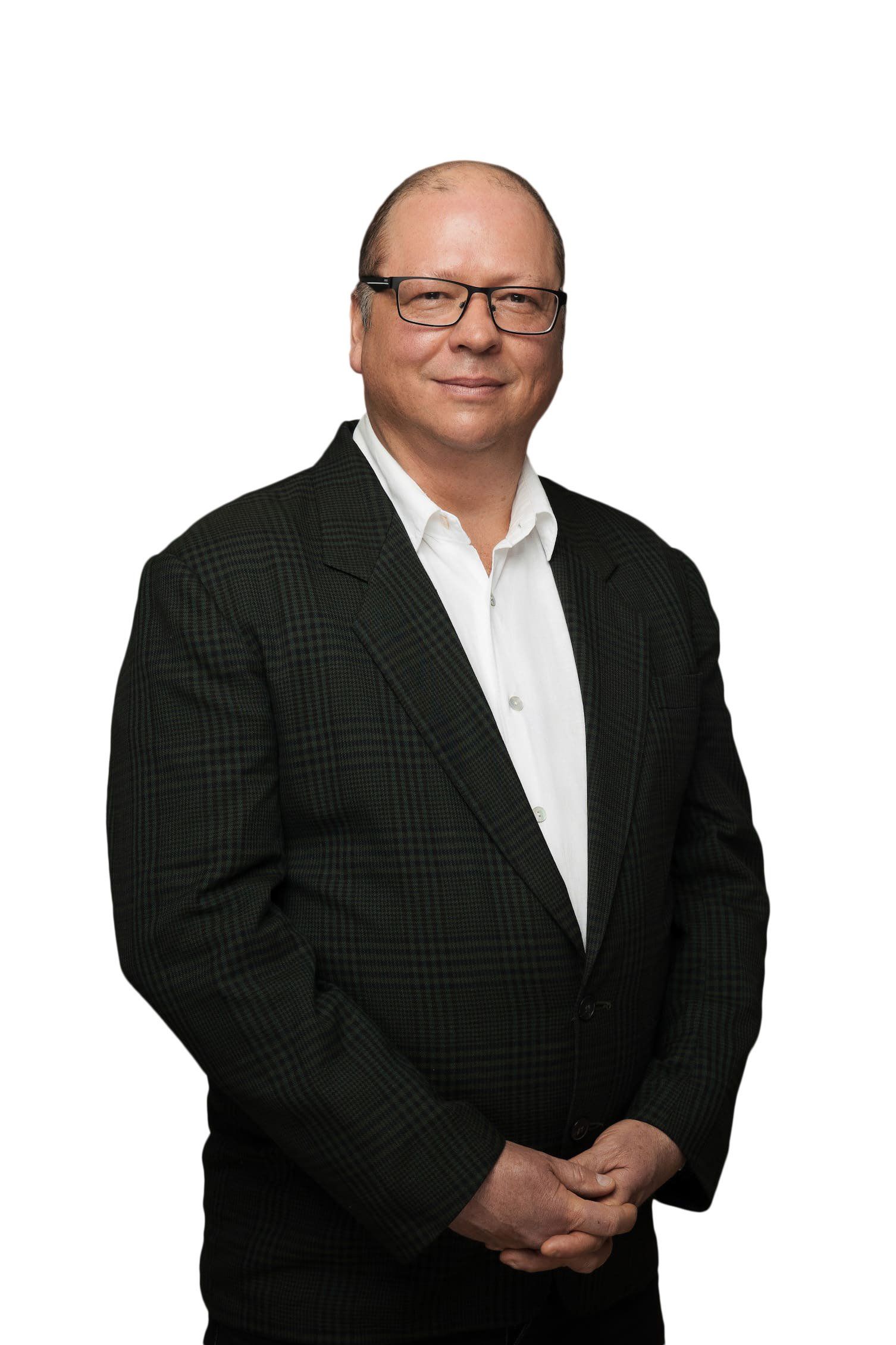 A man in a suit and glasses is standing with his hands folded.