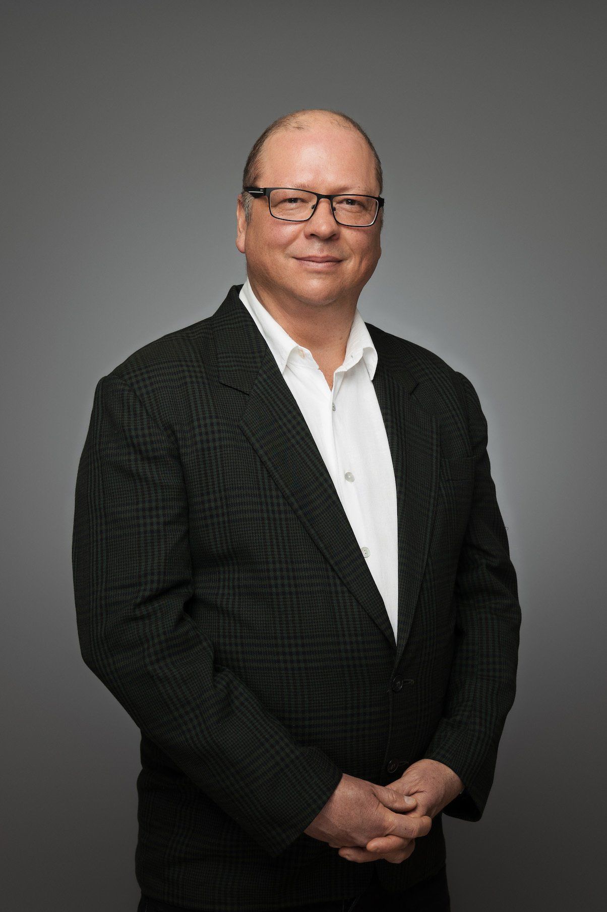 A man in a suit and glasses is standing with his hands folded.