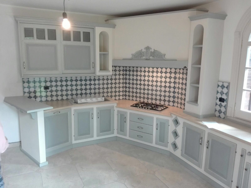 Cucina bianca con mobili azzurri, paraschizzi decorato e pavimento piastrellato in una stanza vuota.