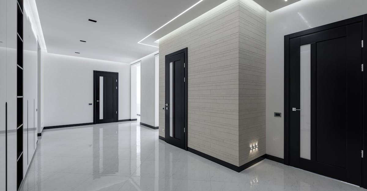 Corridoio di un appartamento moderno con pareti bianche, pavimento lucido, porte nere e faretti a incasso sul soffitto.