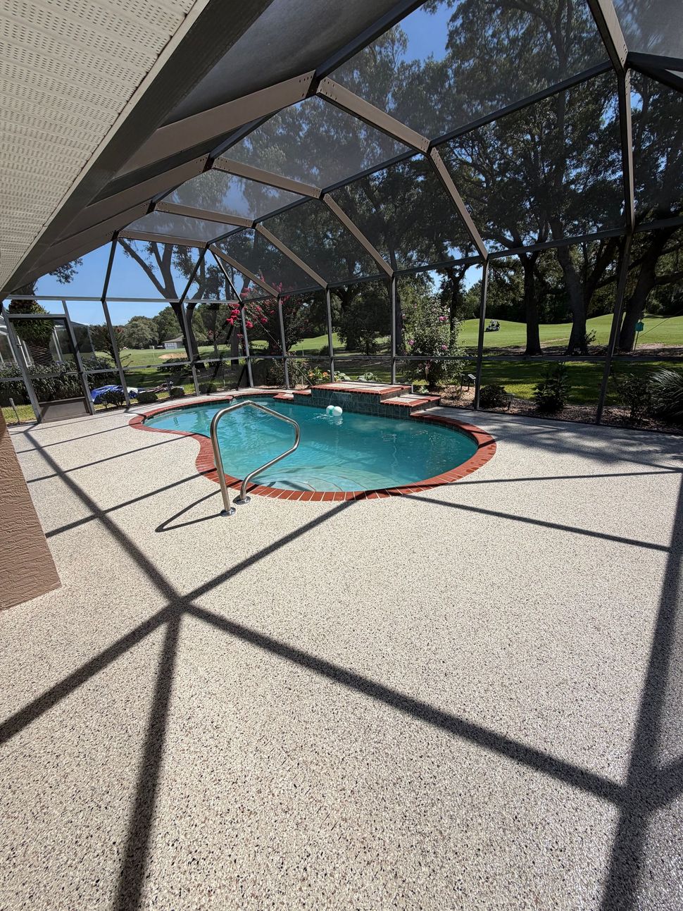 Screened-in patio with a small turquoise pool and sunlit paved deck under trees
