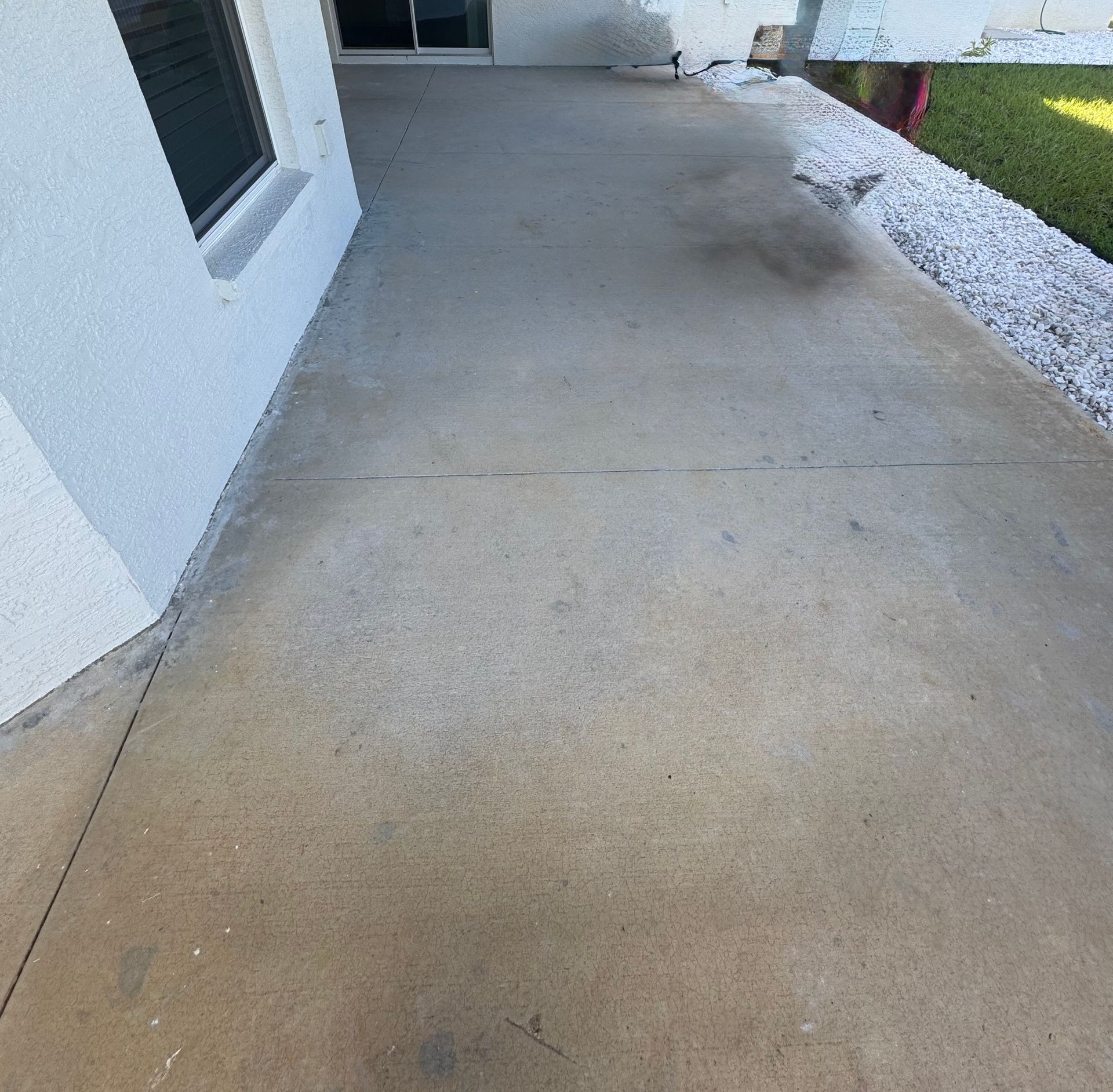 A concrete walkway leading to a house with a window.