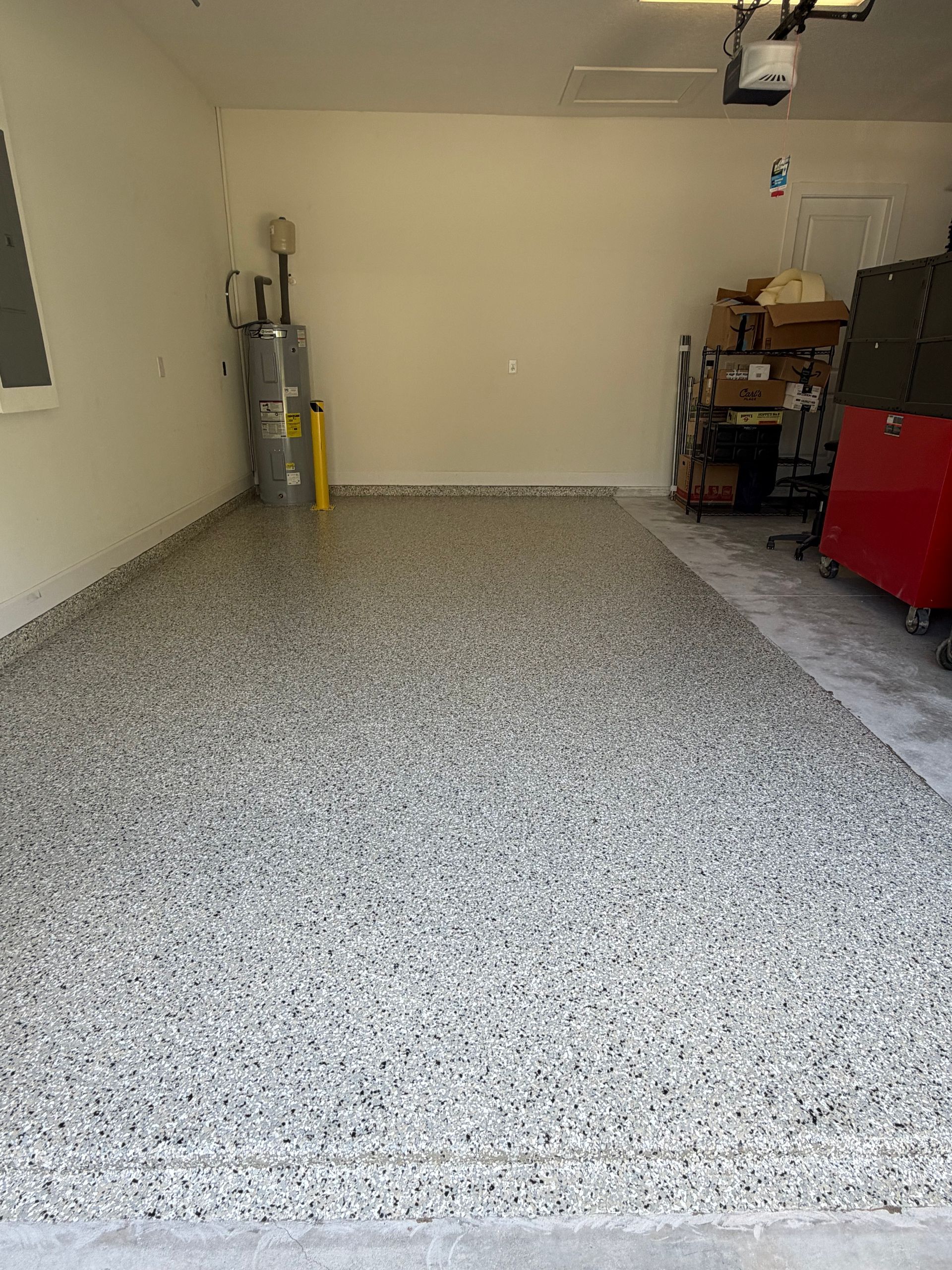 Empty garage with speckled epoxy floor, beige walls, and storage items along the sides.