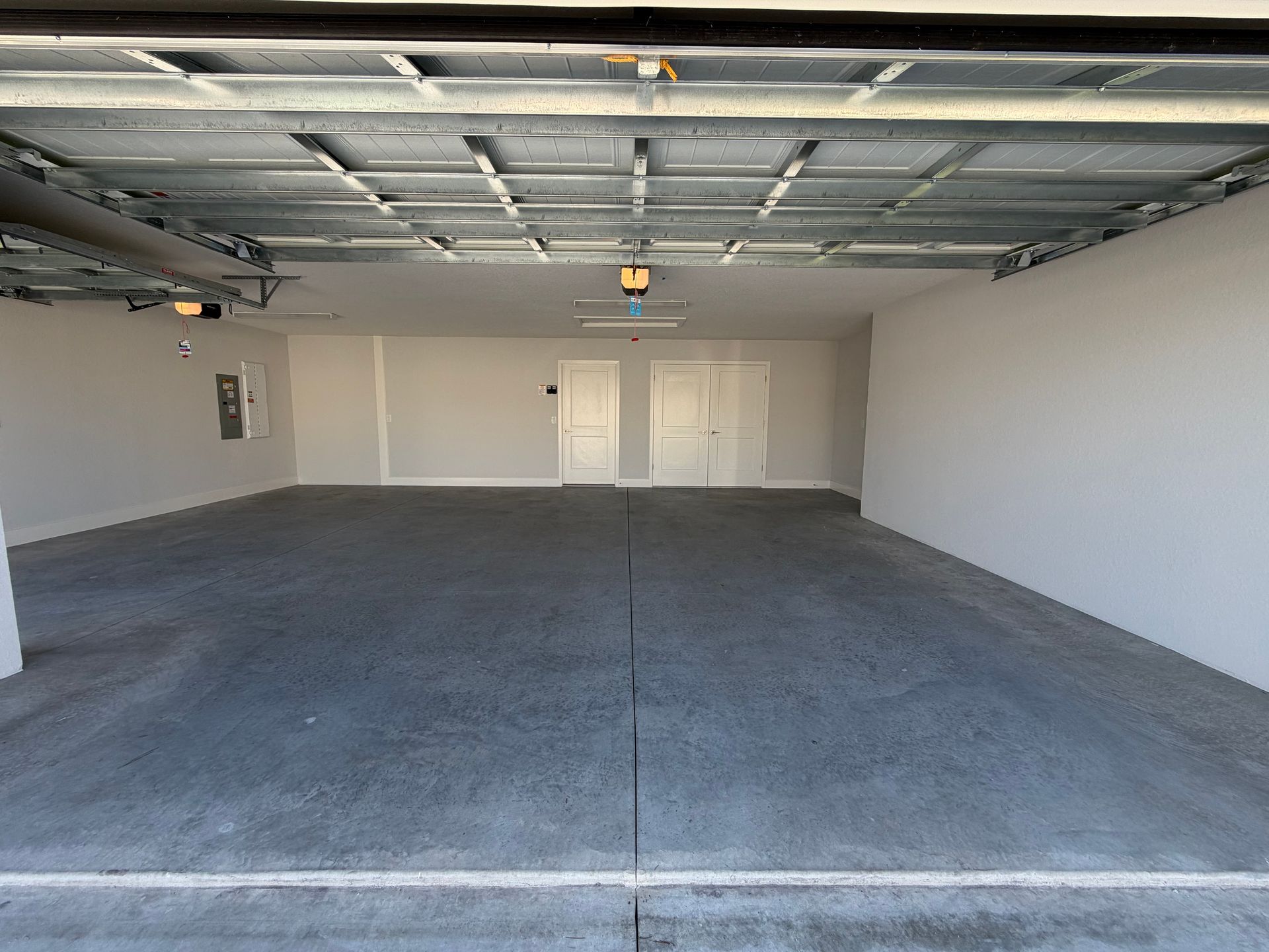 Empty residential garage interior with gray floor, white walls, and exposed ceiling.