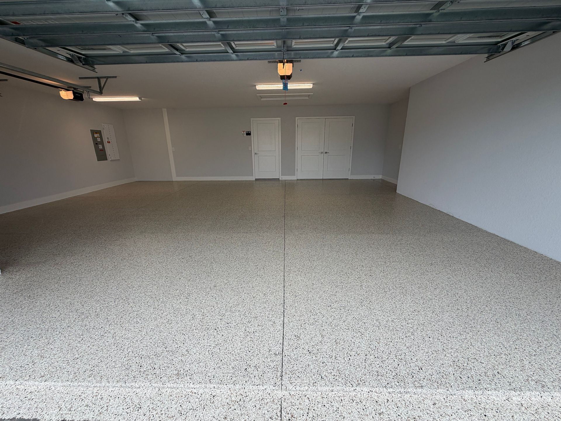 Empty garage with speckled floor, white walls, and ceiling lights.