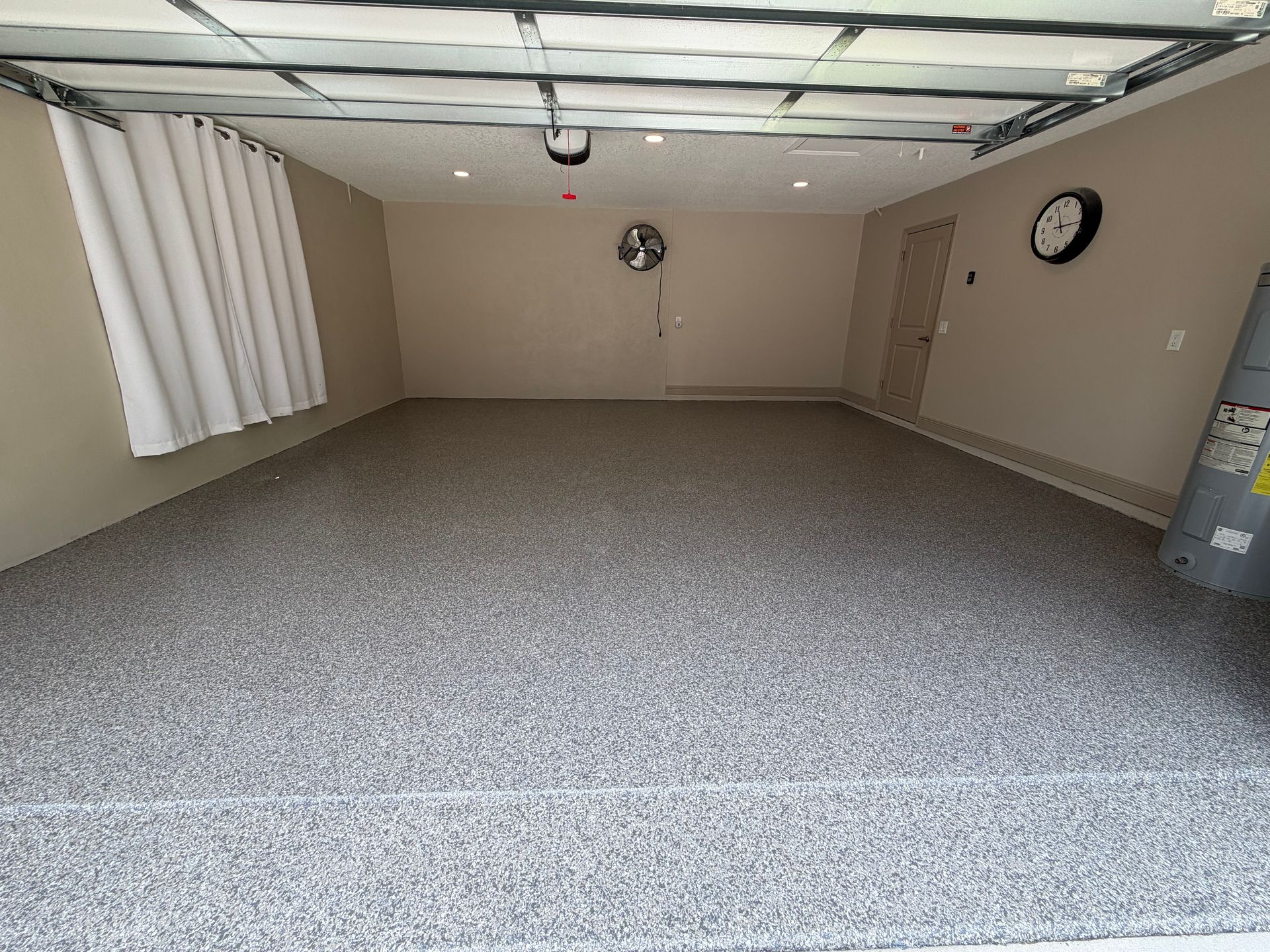 Empty beige basement room with speckled carpet, drop ceiling, and wall clock