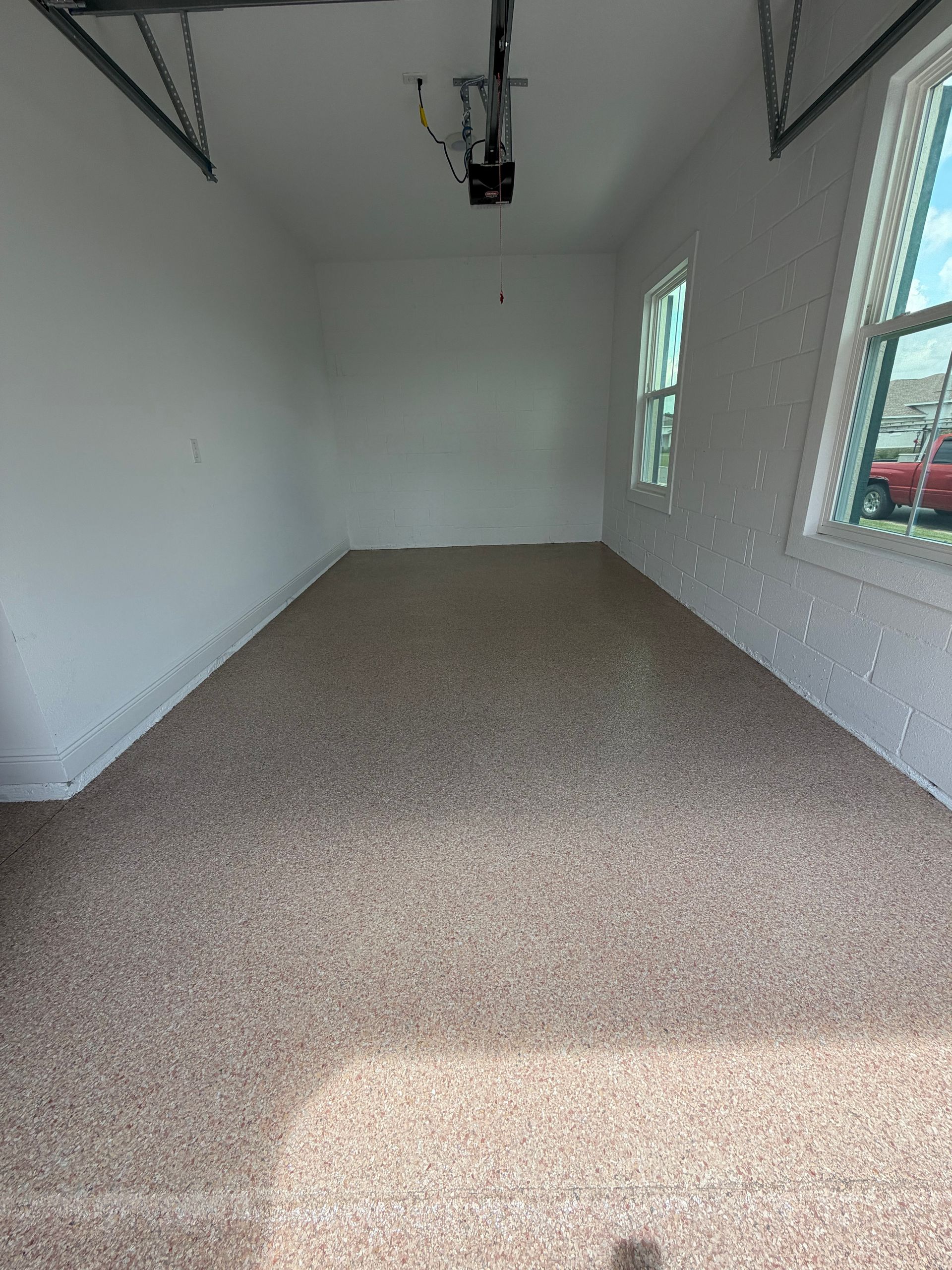 Empty white garage interior with beige carpet, windows on the right, and a garage door opener overhead