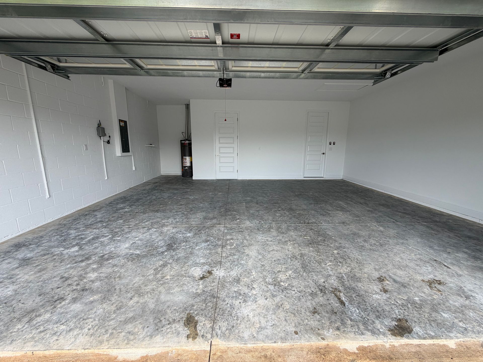 Empty residential garage with concrete floor, white walls, and overhead door tracks