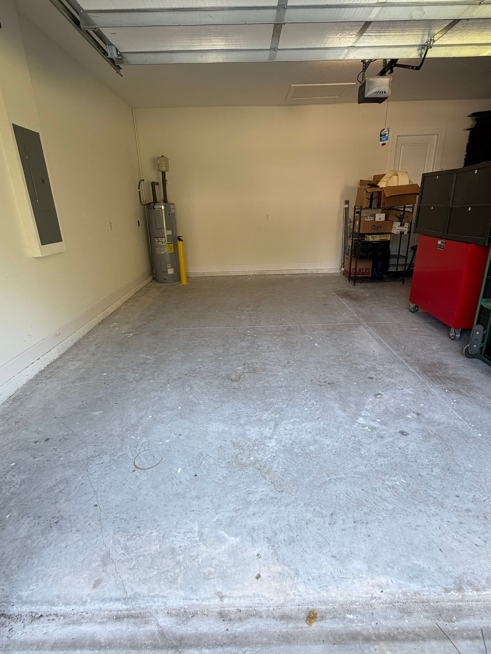 Empty garage with concrete floor, beige walls, overhead door track, and storage items along the sides.