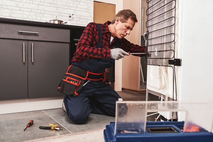 Worker kneeling on floor, repairing a wall-mounted radiator in a kitchen with tools nearby