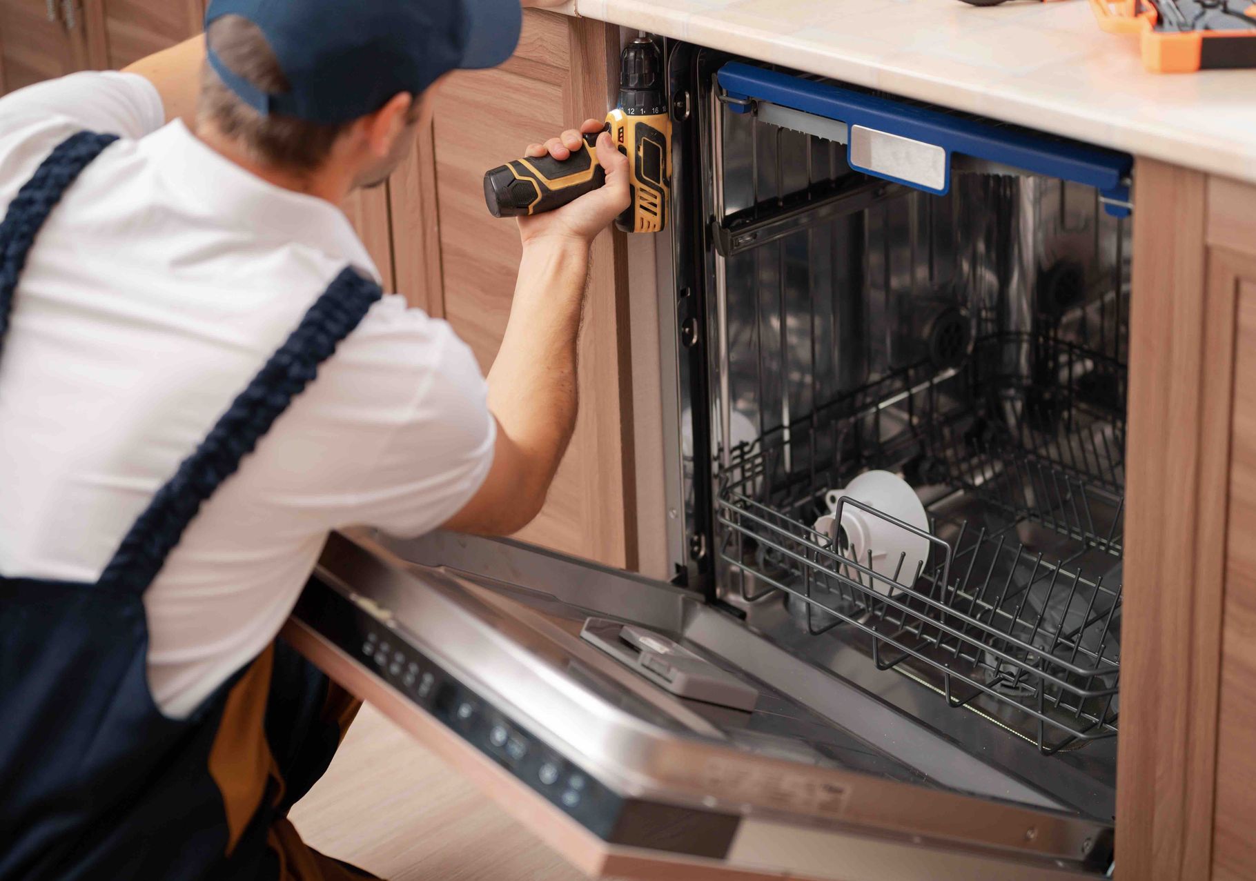 Technician installing a dishwasher under a kitchen counter with a drill