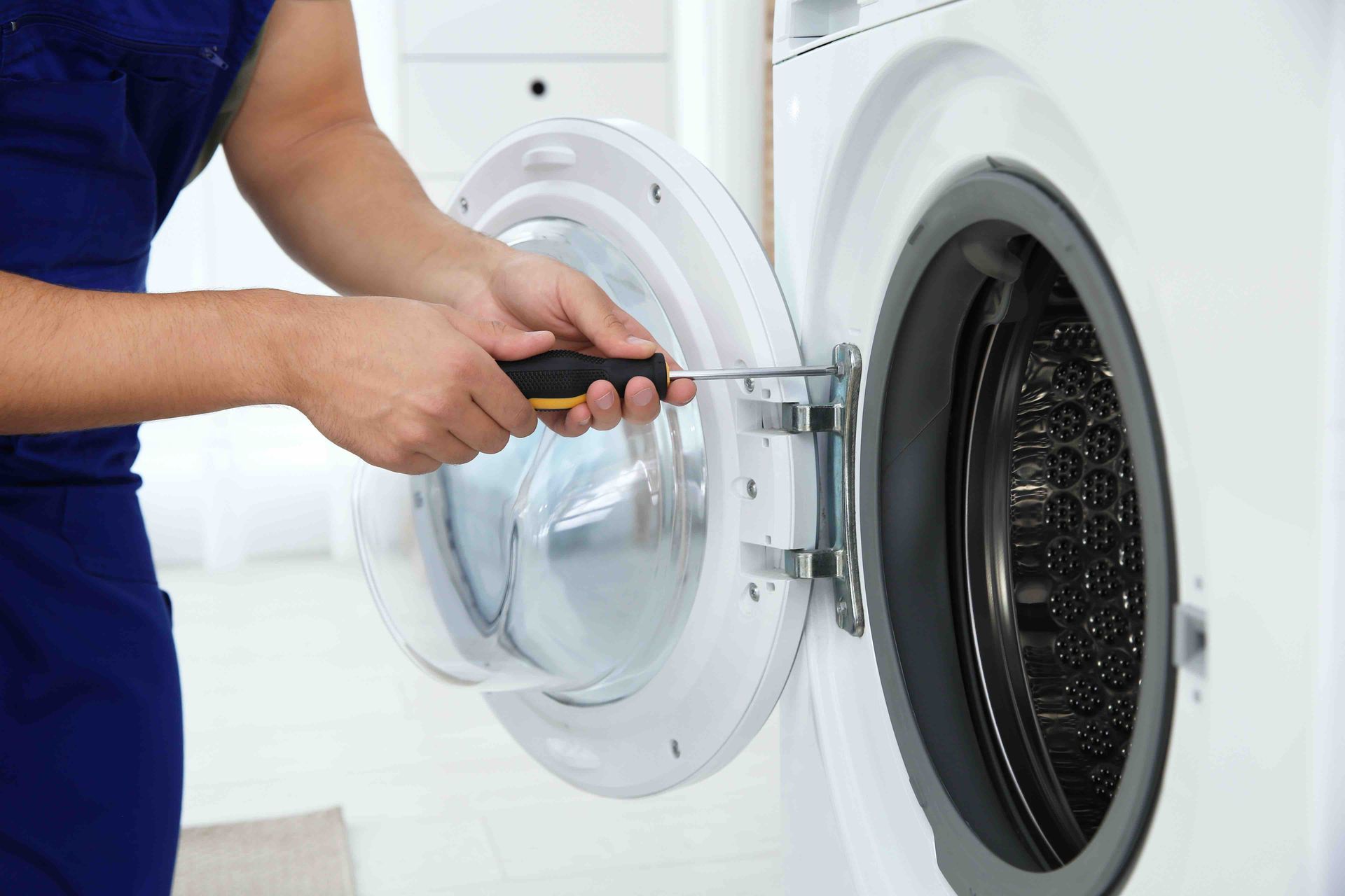 Technician using a screwdriver to repair an open front-loading washing machine in a laundry room