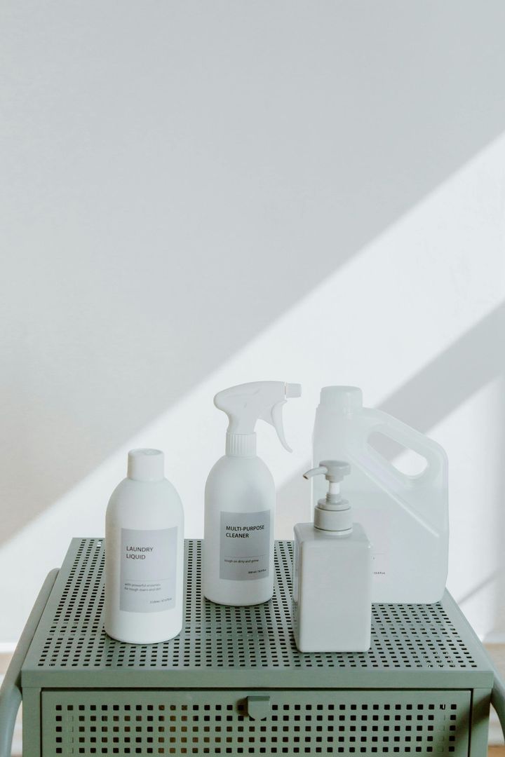 White cleaning bottles and spray containers on a green perforated stool in sunlight.