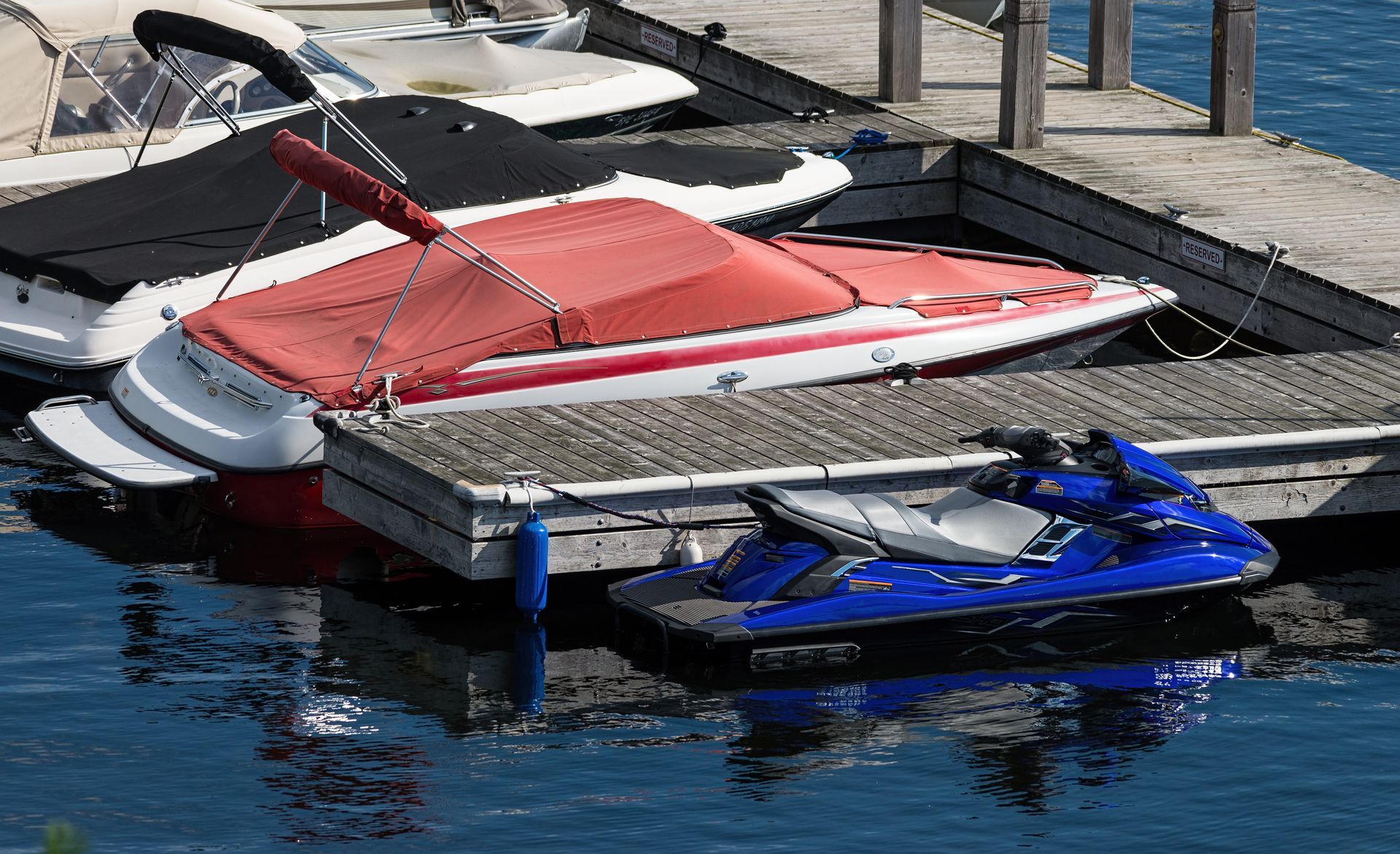 A red boat is sitting on a dock next to a blue jet ski