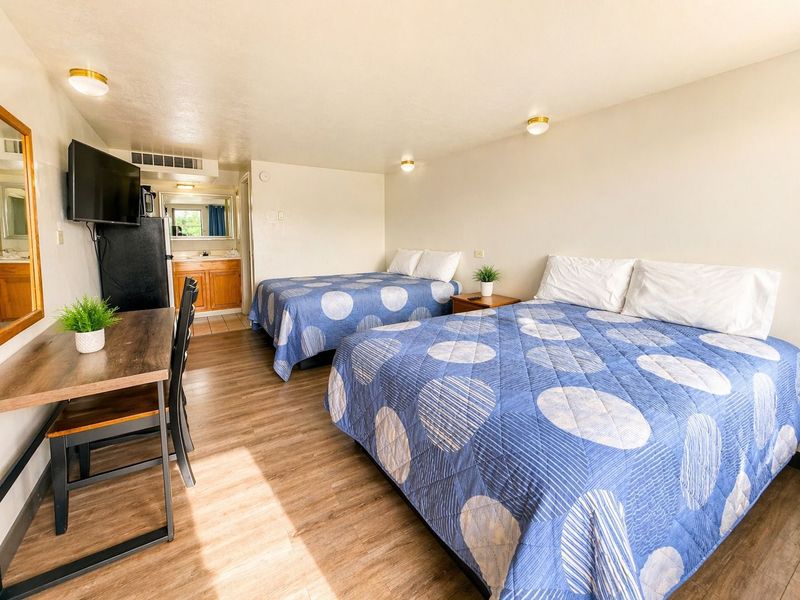 Bright hotel room with two queen beds, wood floor, TV, and a small desk by the window.