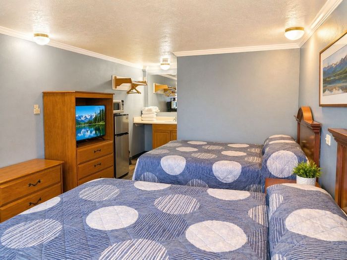 Hotel room with two beds, wooden dresser, TV, and small kitchenette in gray decor