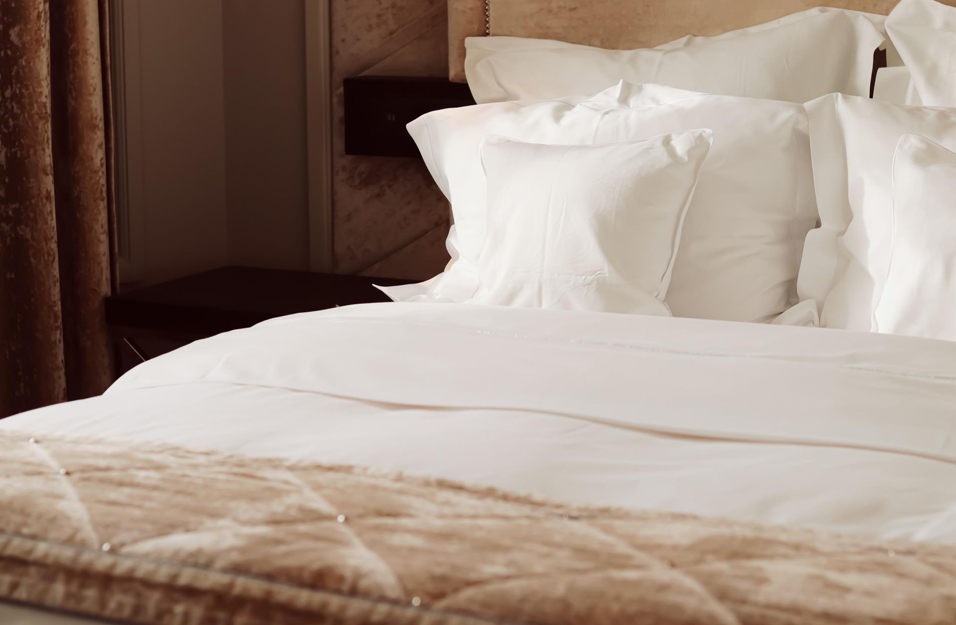 Neatly made bed with white pillows and beige blanket in a softly lit bedroom