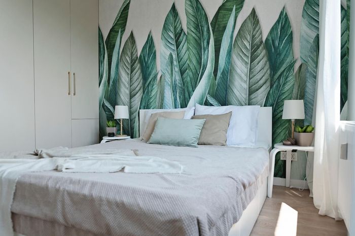 Bright bedroom with a white bed, leafy green mural, and soft natural light from large windows