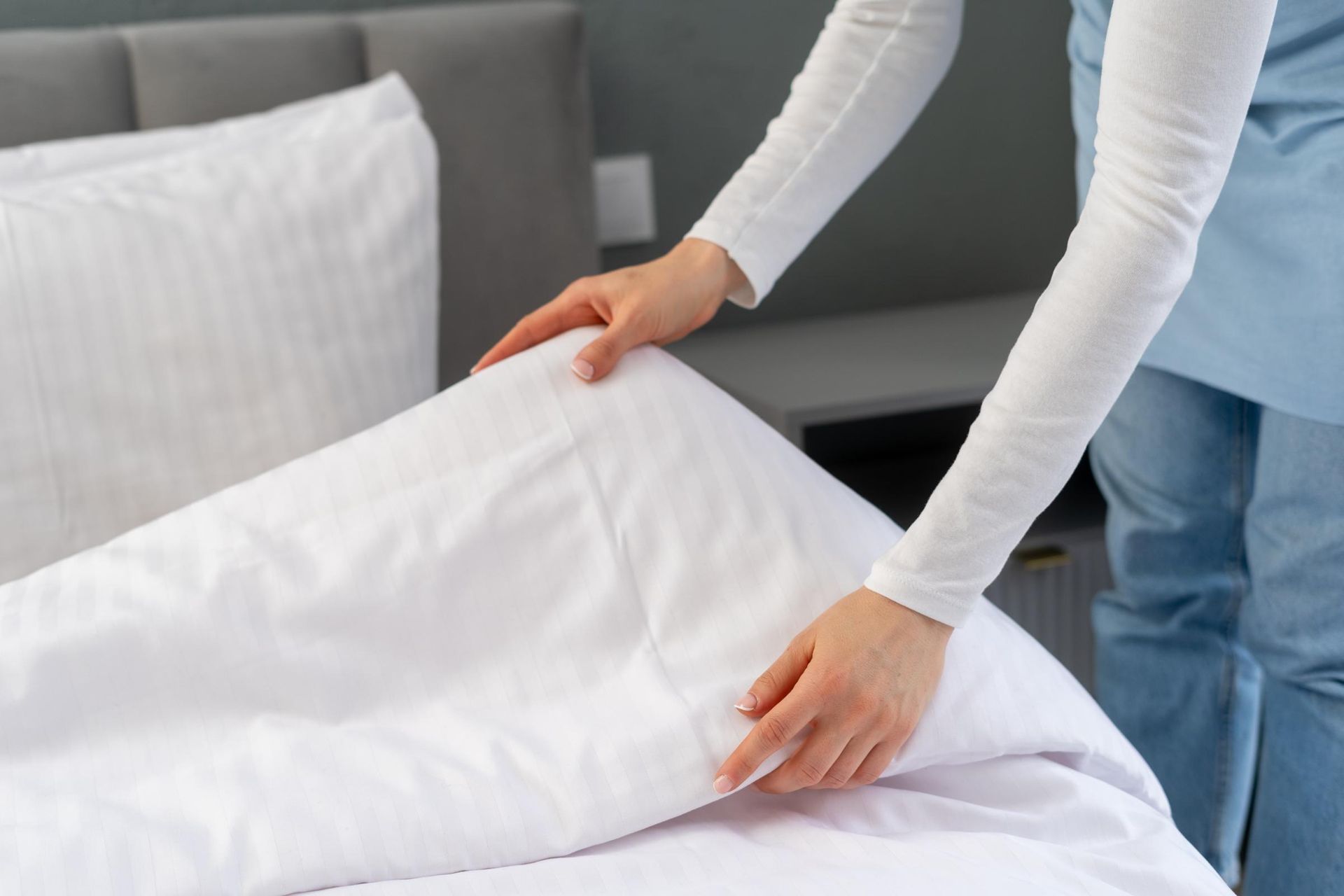 Person making a bed with white sheets in a bedroom