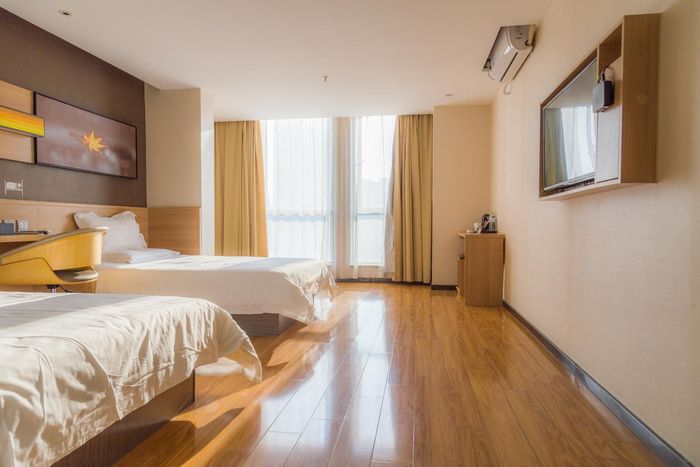 Bright hotel room with two beds, wood floors, and sunlight through large windows.