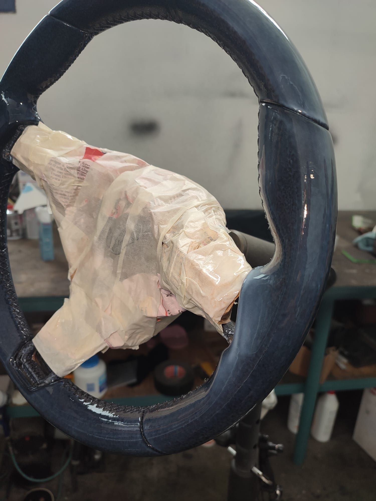 Volante nero avvolto in nastro adesivo di plastica, con uno sfondo di officina.