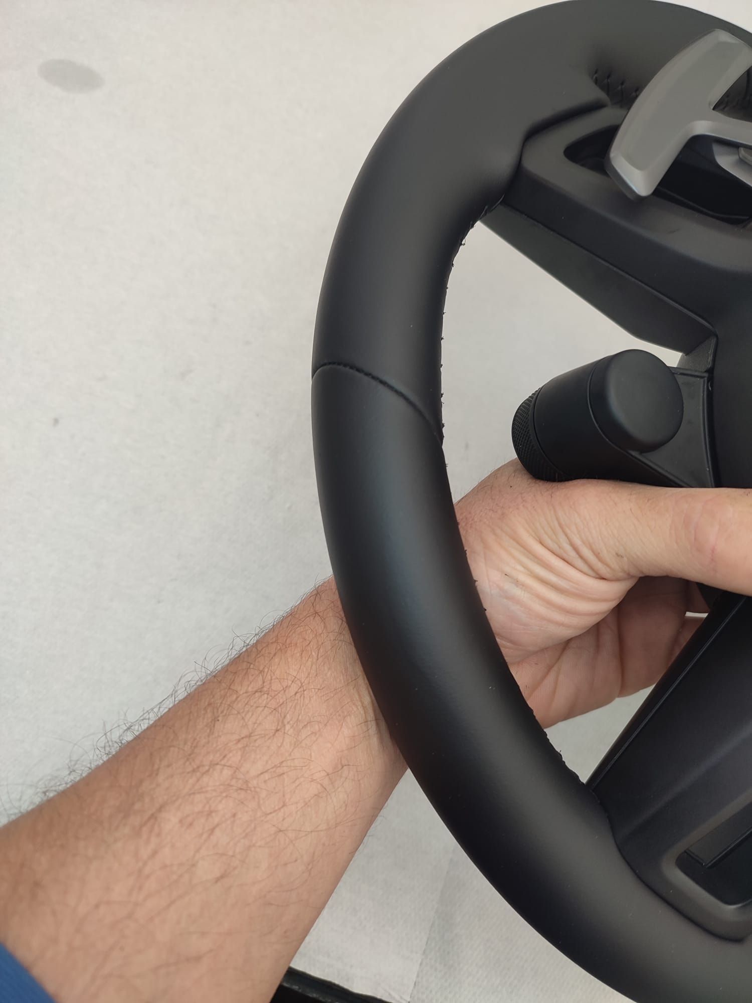 Mano che impugna un volante/controller nero su sfondo grigio