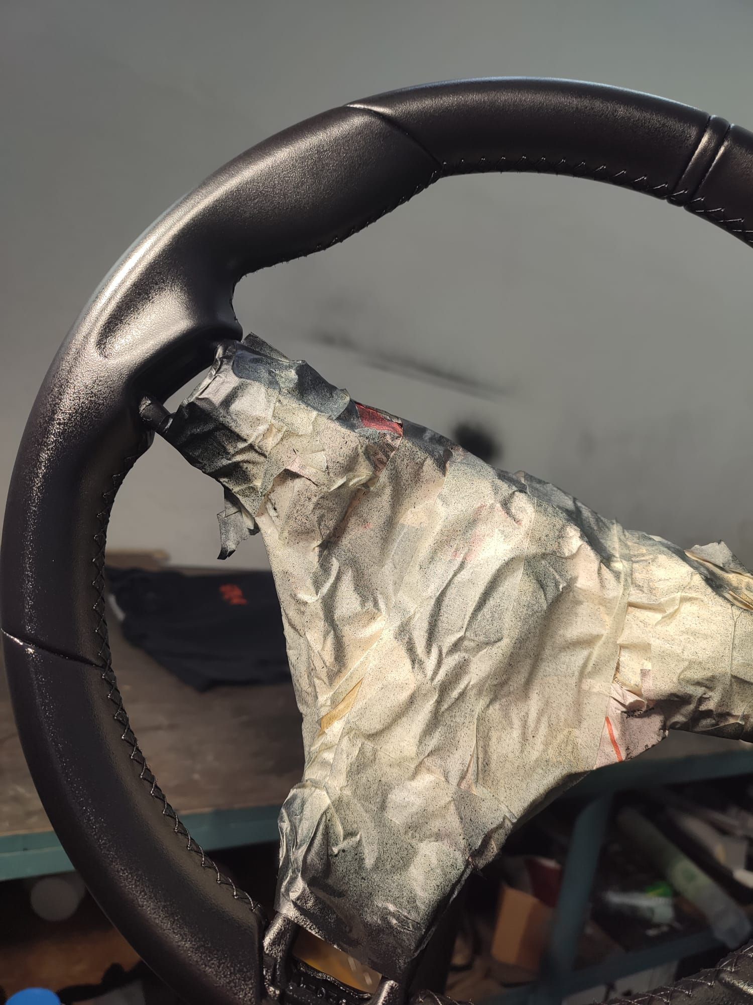 Primo piano di un volante usurato avvolto in nastro adesivo grigio strappato, con l'interno di un'auto sfocato sullo sfondo.
