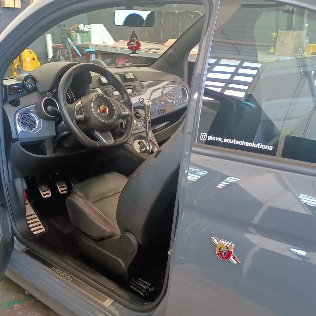 Interno di un'auto grigia con la portiera del conducente aperta, che mostra il volante, i sedili neri e il cruscotto.