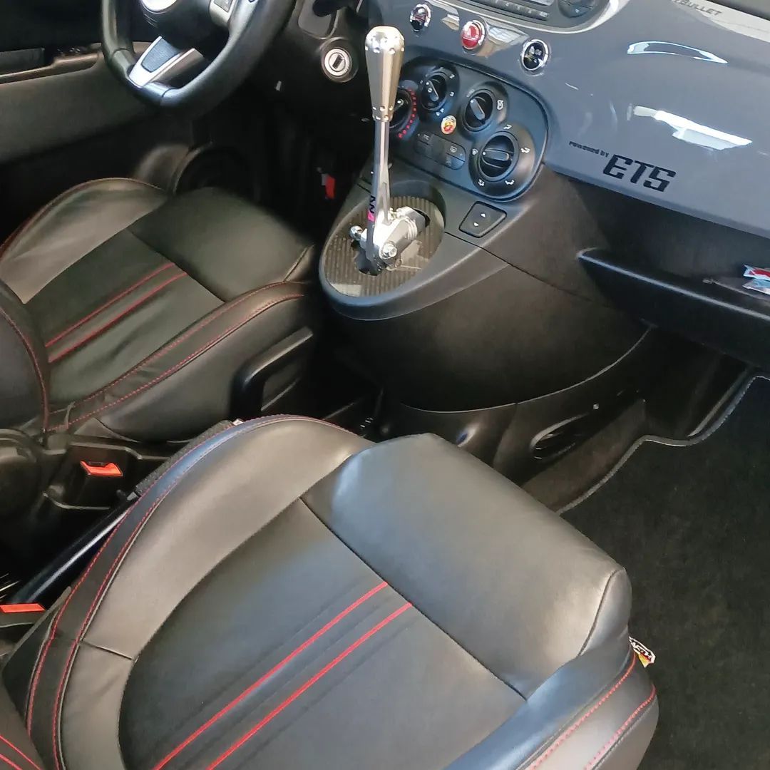 Interni dell'auto con sedili in pelle nera, cuciture rosse e cambio manuale.