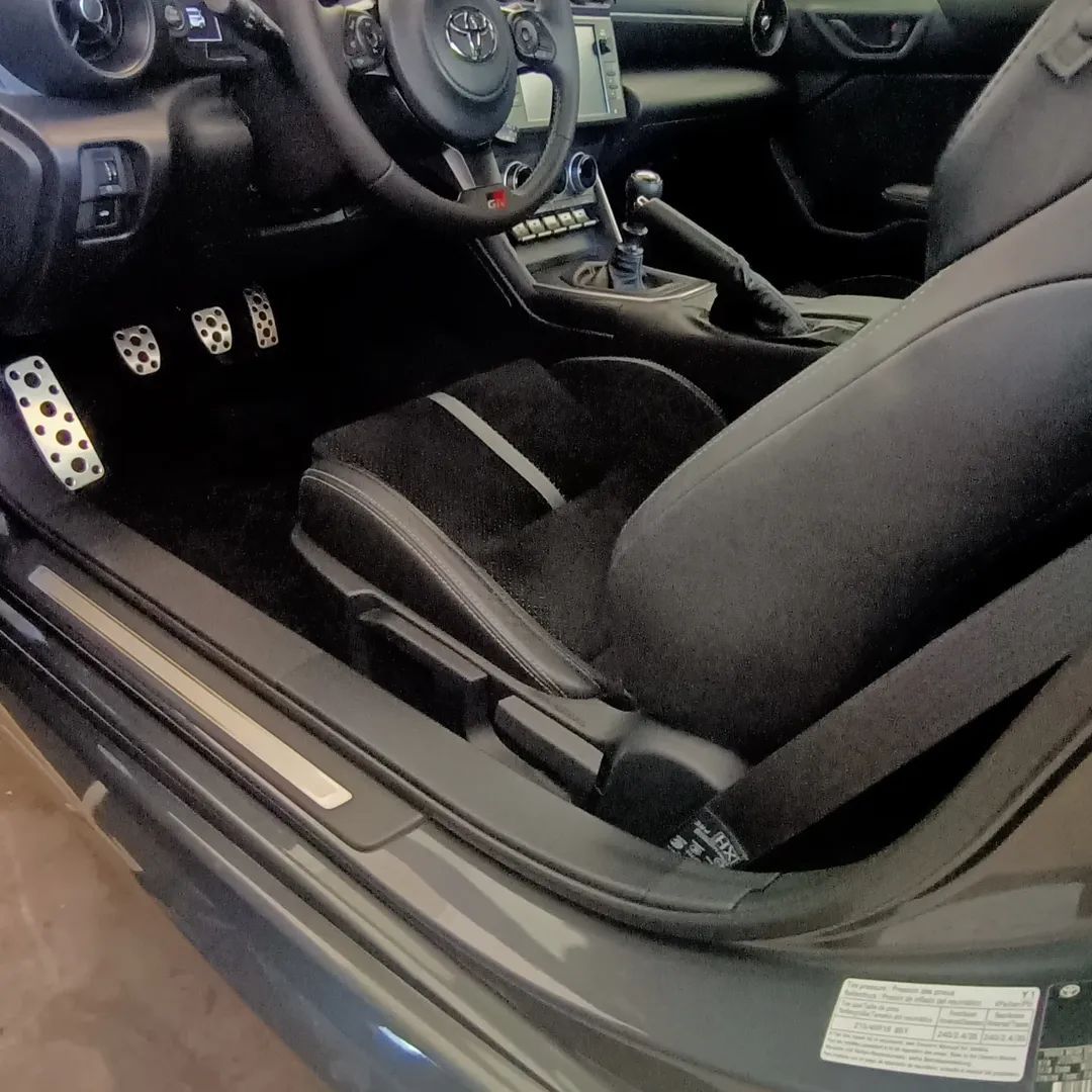 Interni dell'auto con sedili da corsa neri, cambio manuale e copripedali in metallo.