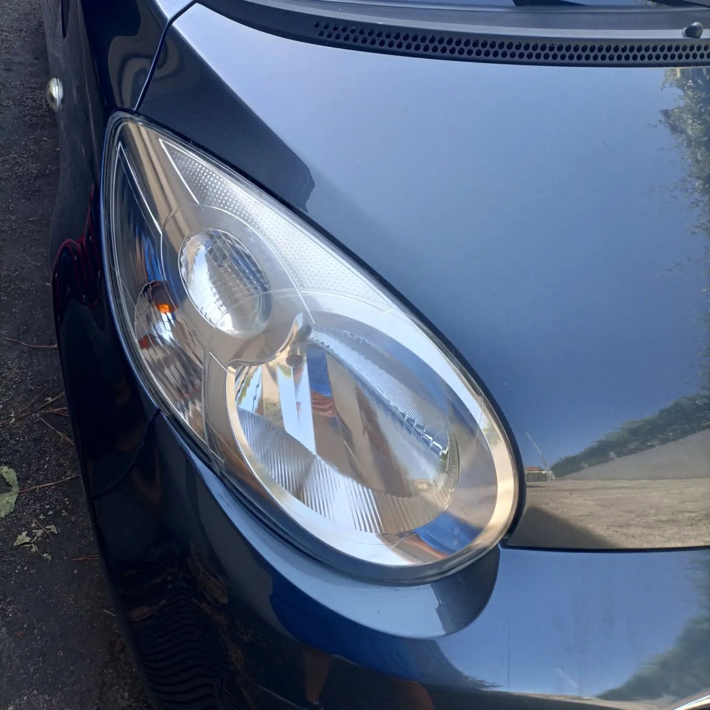 Primo piano del faro anteriore e del cofano di un'auto blu alla luce del sole.