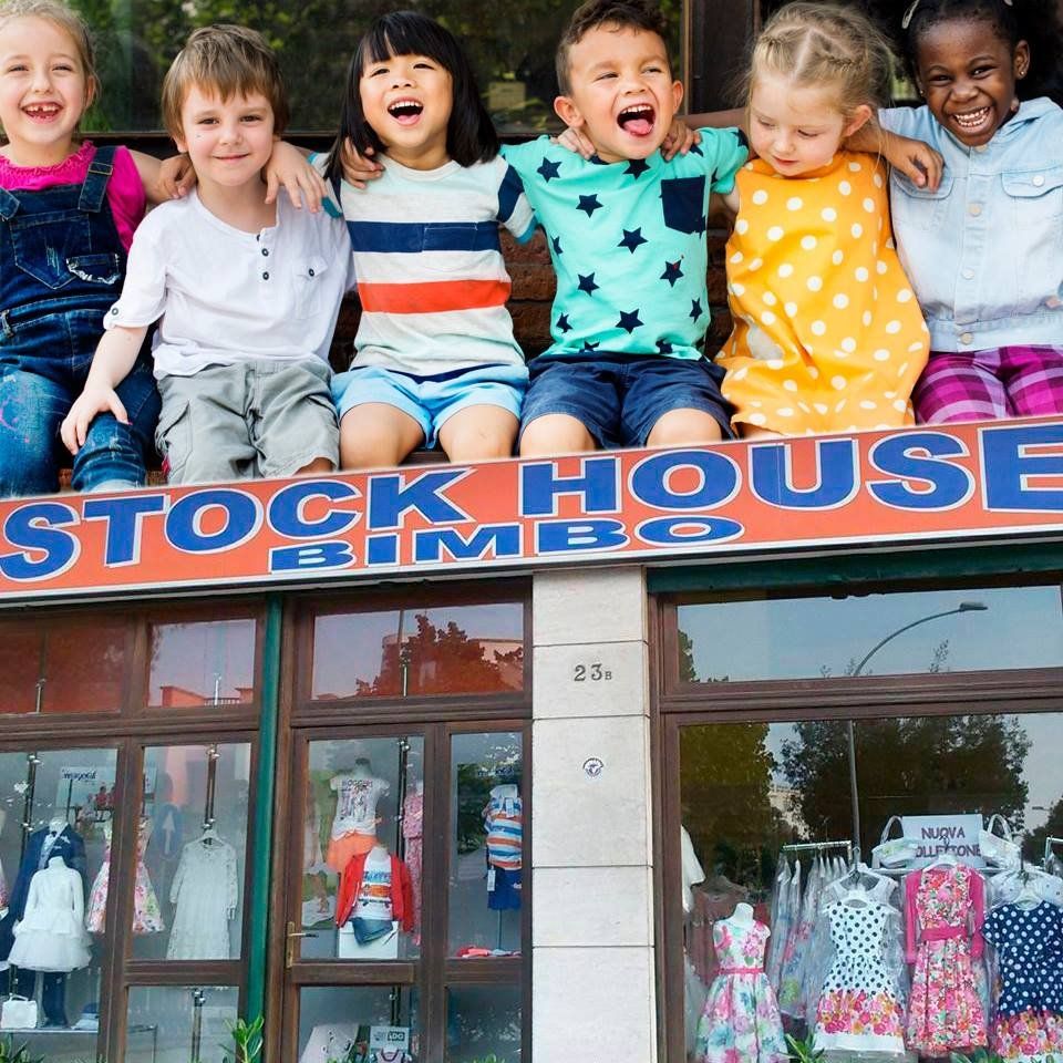 Bambini che sorridono e si abbracciano sopra un negozio di abbigliamento per bambini con vetrine colorate.