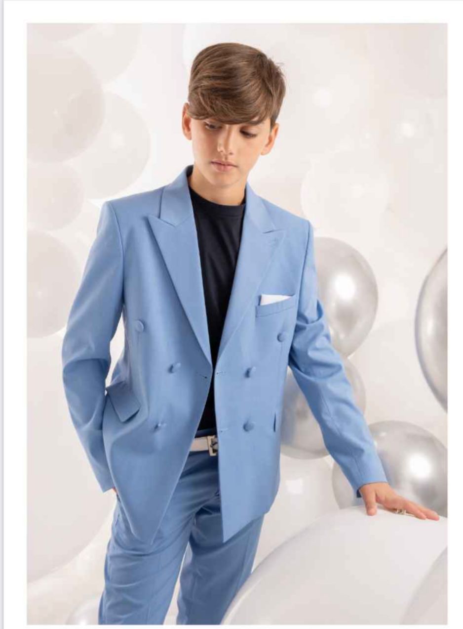 Ragazzo in abito azzurro, in piedi vicino a palloncini; indossa una camicia nera, cintura bianca e fazzoletto da taschino.