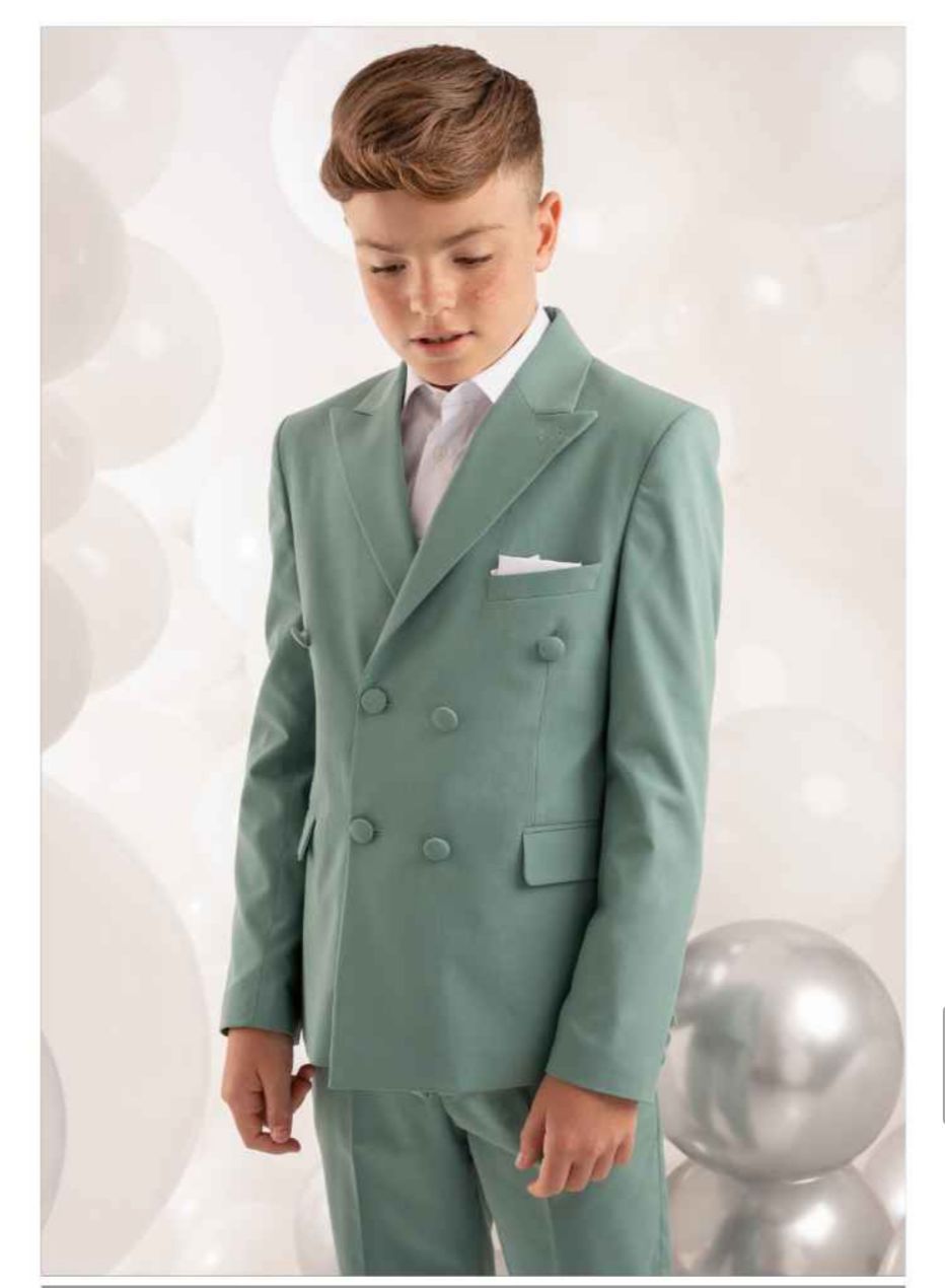 Ragazzo con un abito doppiopetto verde salvia e una camicia bianca, che guarda in basso, davanti a palloncini argentati.