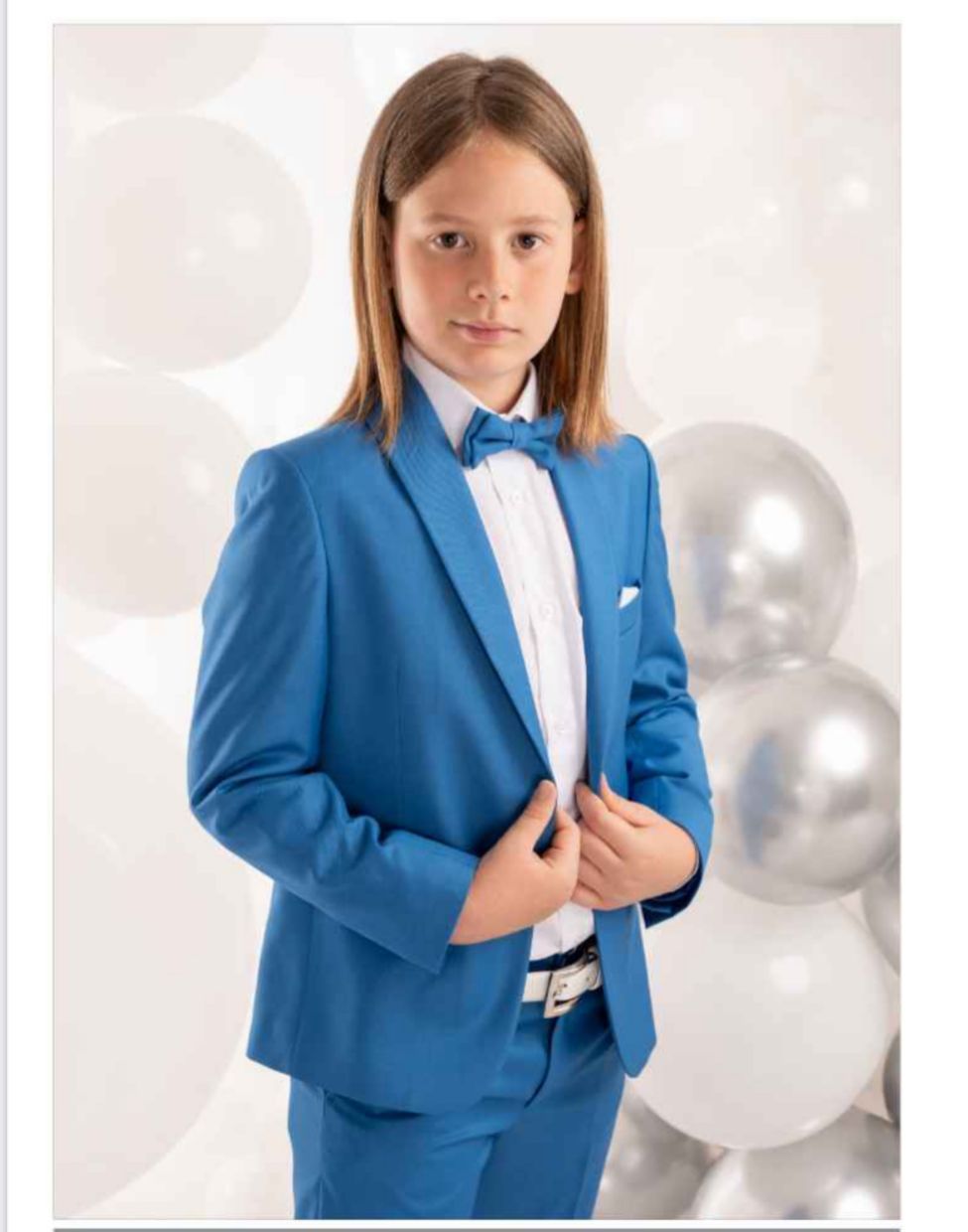 Ragazzo in abito blu e papillon in posa su uno sfondo di palloncini.