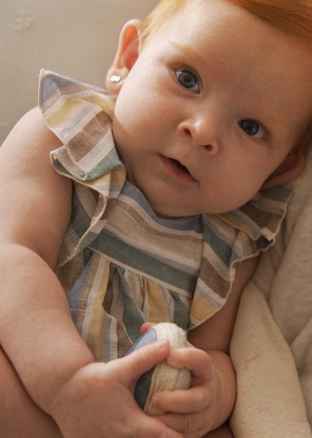 Bambino con i capelli rossi e gli occhi azzurri, che indossa un vestito a righe e tiene in mano un giocattolo.