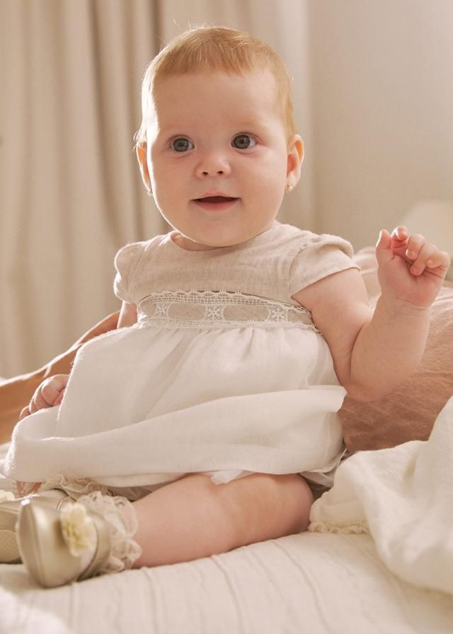 Un bambino con un vestito bianco è seduto sul letto e sorride.