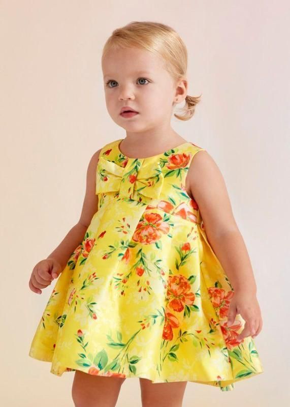 Ragazza con un vestito giallo a fiori e un fiocco, che guarda leggermente di lato.