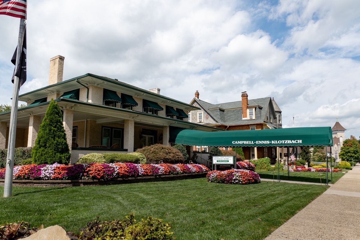 Funeral Home with a green entrance canopy, landscaped lawn, and colorful flower beds.