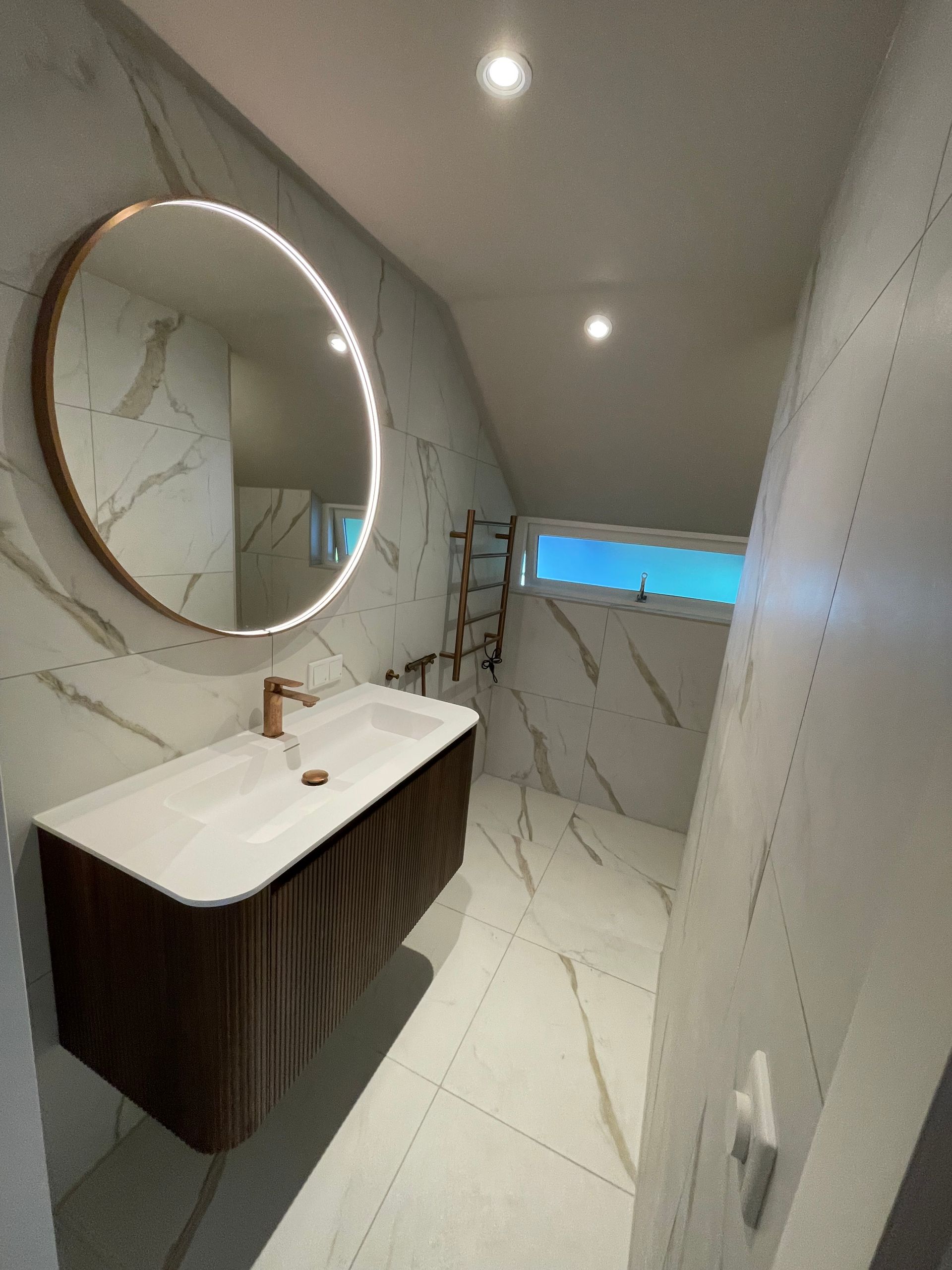 Moderne badkamer met verlichte ronde spiegel en afgewerkte elektra