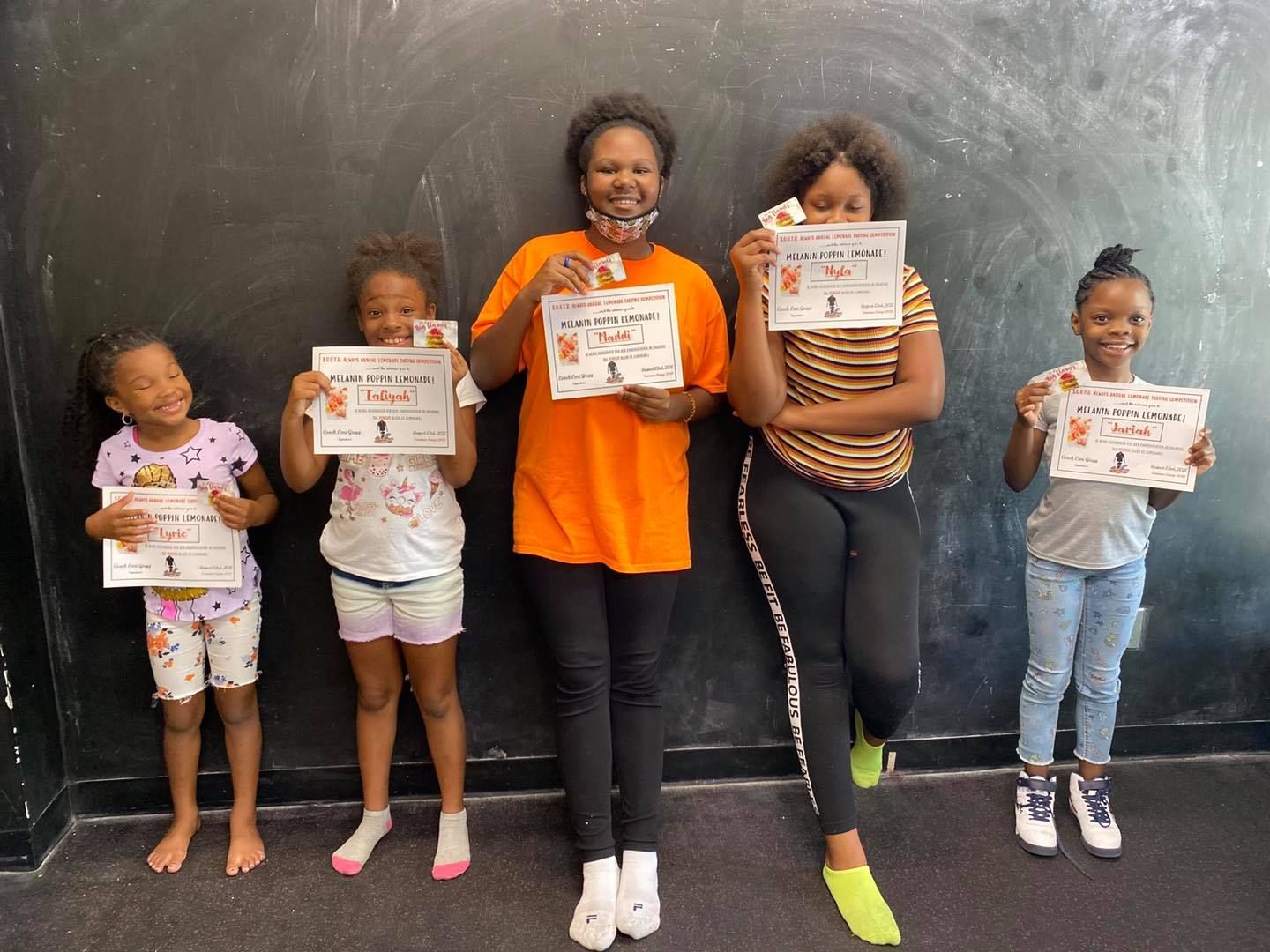 Five people standing in front of a black wall, holding up certificates, smiling, and wearing casual clothing.
