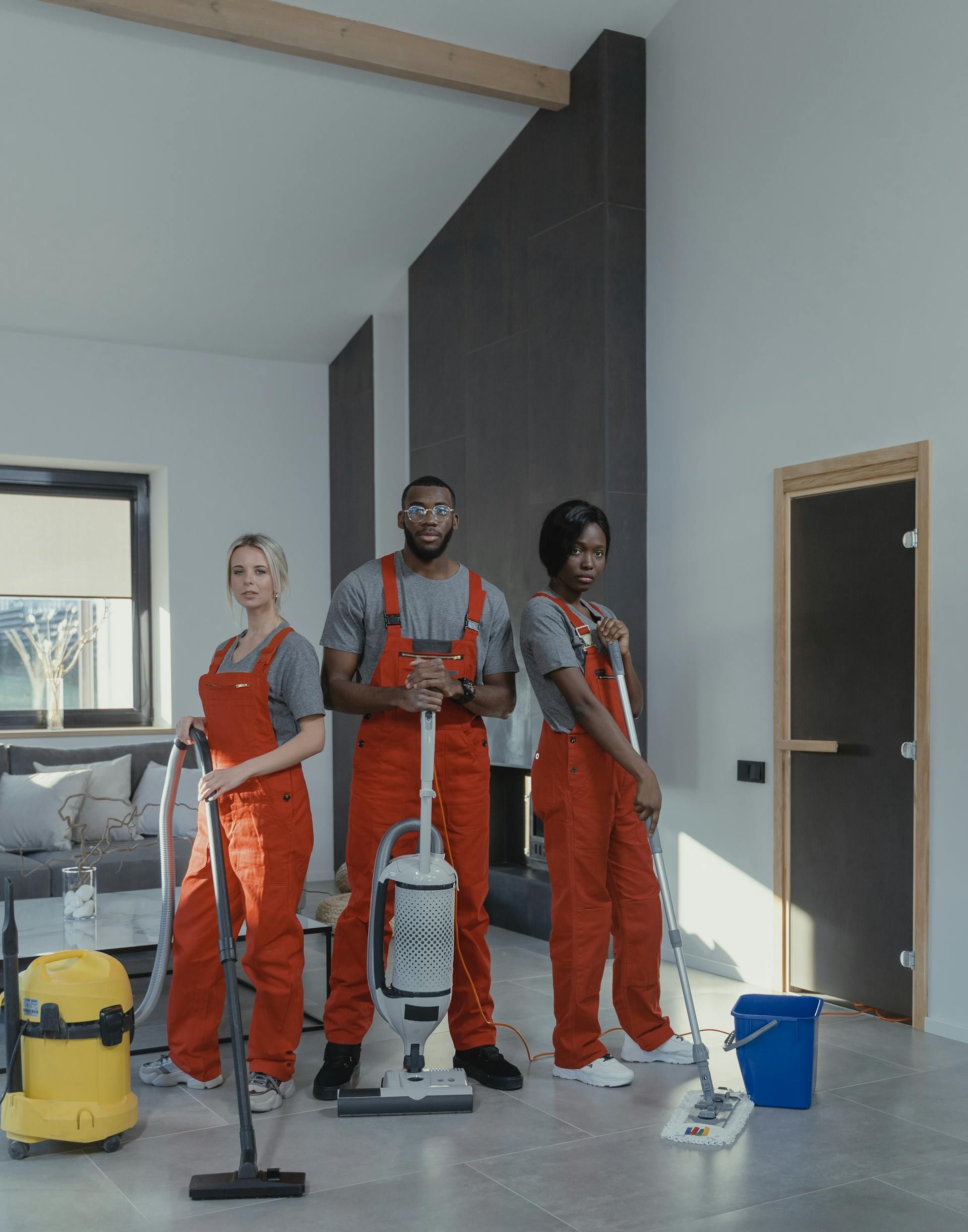 A group of cleaners are standing in a living room with cleaning supplies.