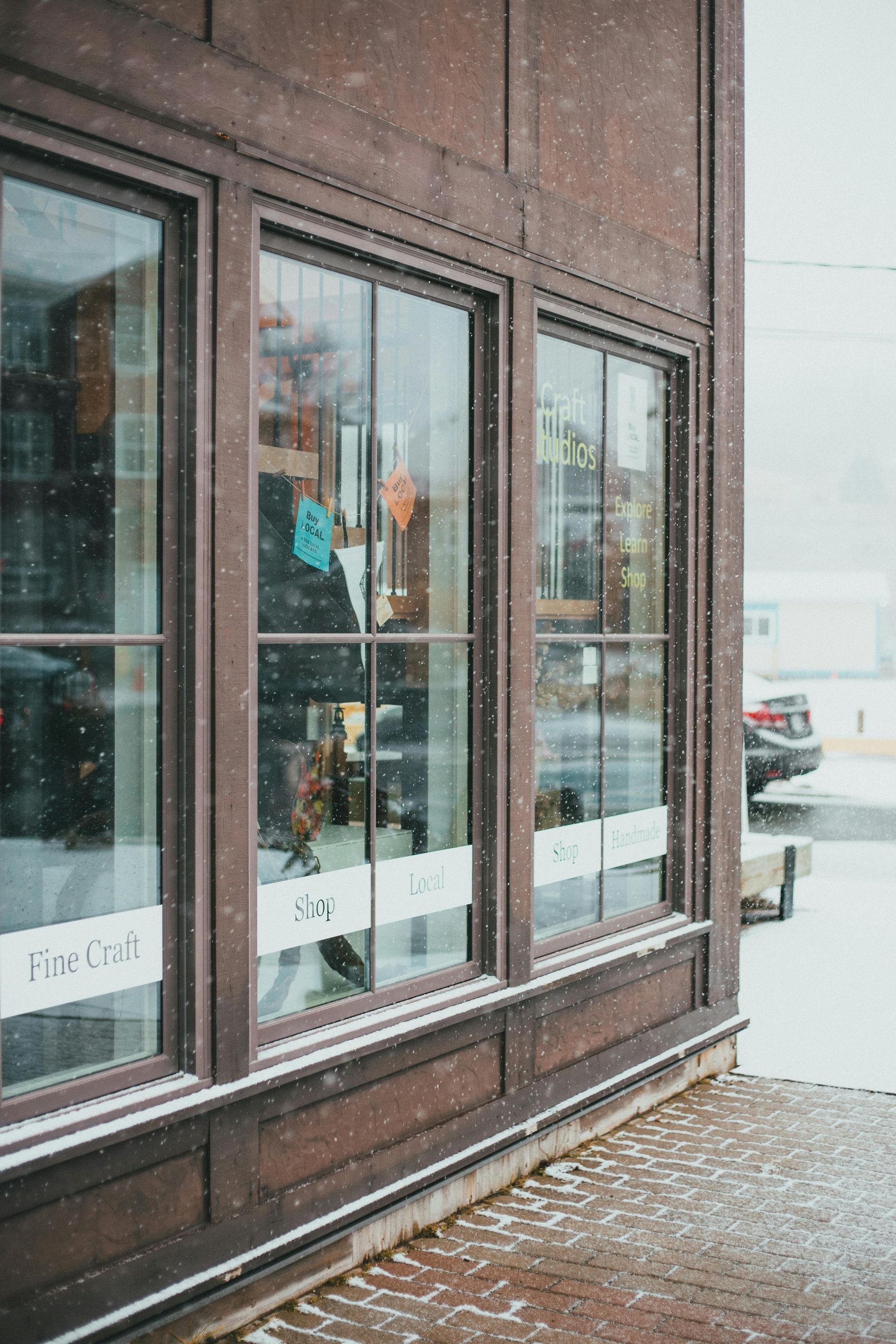 Snowy storefront with large windows and a brick facade on a winter sidewalk.