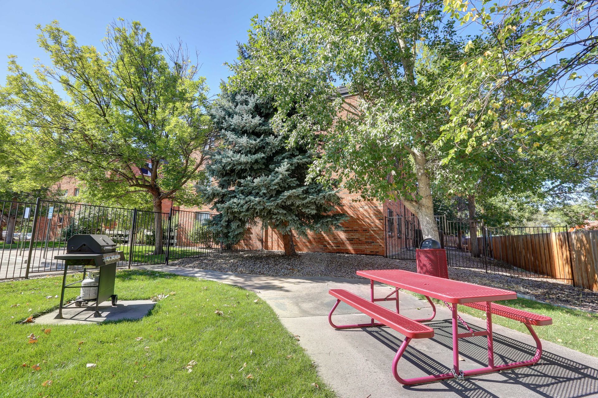 A red picnic table and grill in a park.
