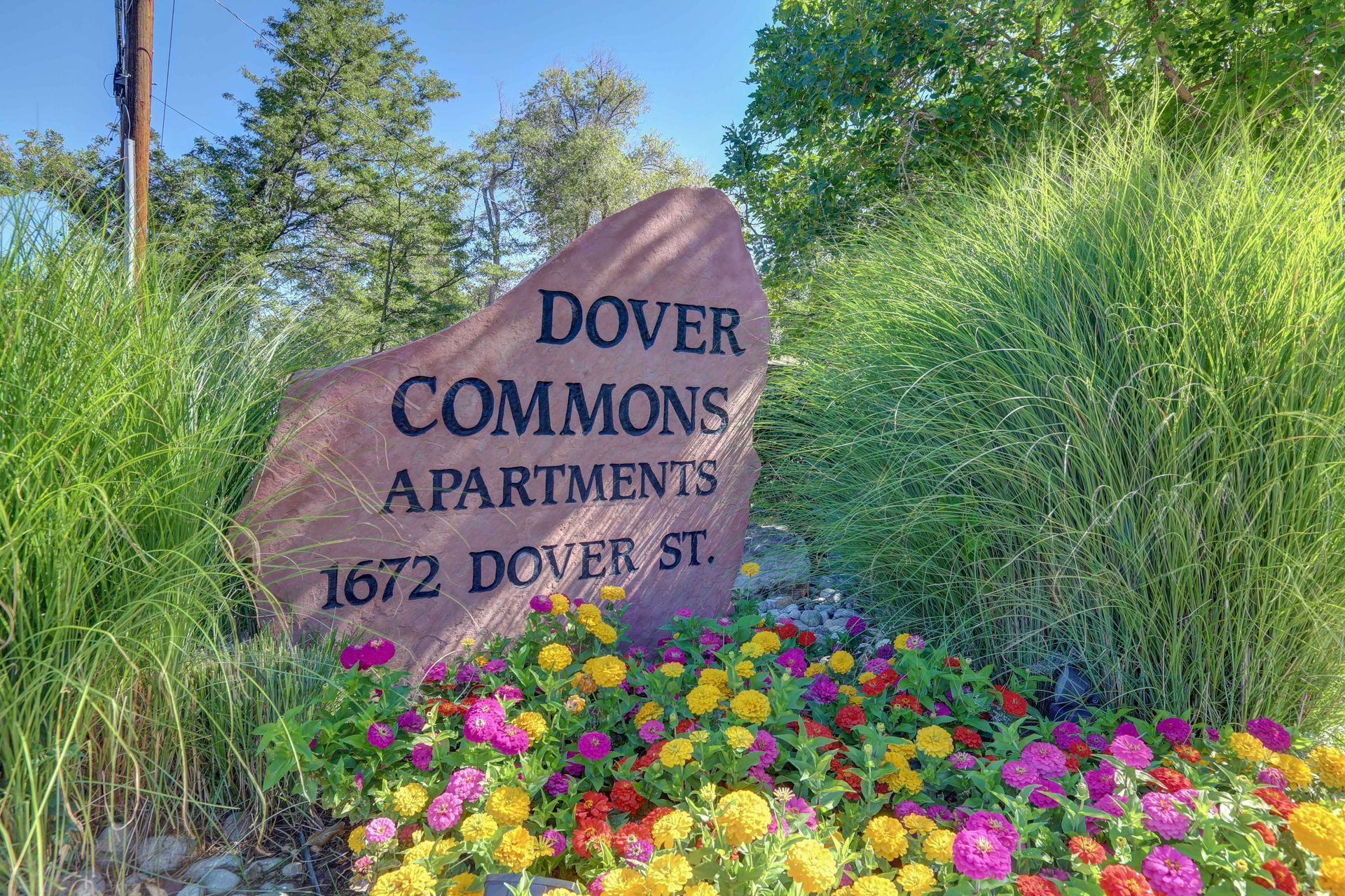 A sign for dover commons apartments is surrounded by flowers.
