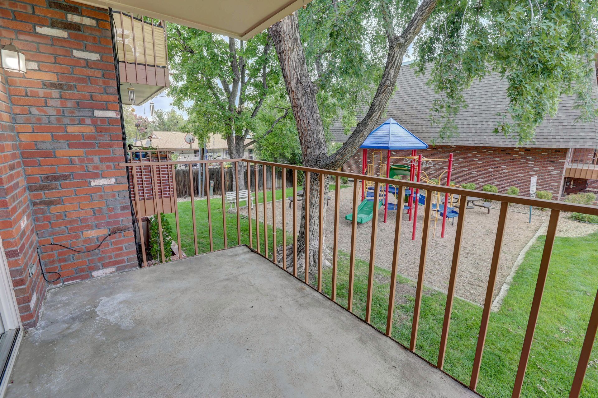 A balcony overlooking a playground with a brick building in the background.