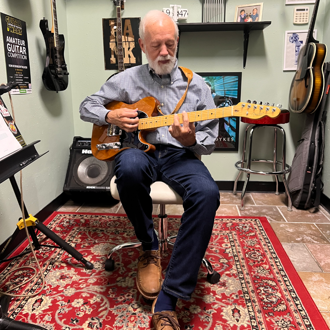 A man is sitting on a chair playing a guitar in a room getting guitar lessons from David Dunavant in Little Rock, AR