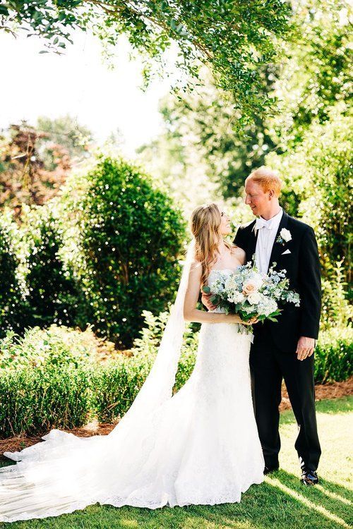 A bride and groom are standing next to each other on a lush green field.