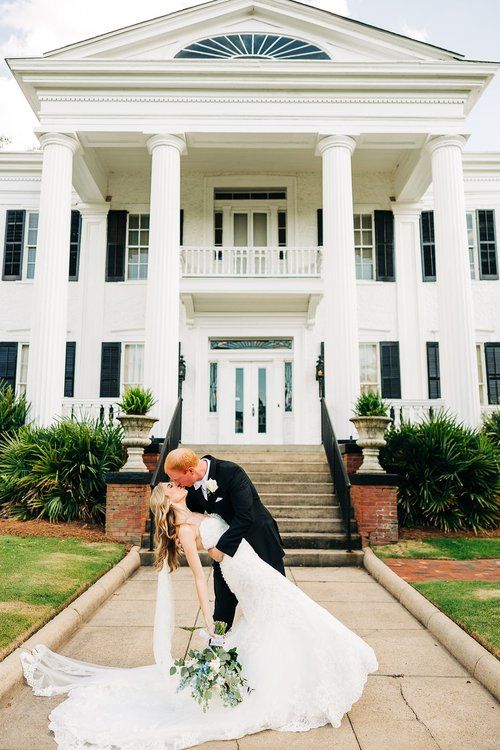 A bride and groom are kissing in front of a large white building.